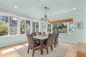 A dining area with a large table, chairs, and a hanging light fixture.