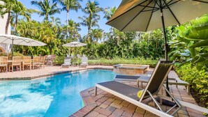 A swimming pool with lounge chairs and umbrellas, surrounded by palm trees and greenery. - Luxury 5BR Gulf-View Home with Private Pool, Spa & High-Tech Entertainment (Captiva)