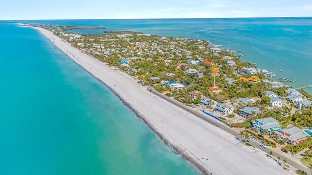 An aerial view of a coastal town with a long sandy beach, clear blue waters, and residential buildings. - Luxury 5BR Gulf-View Home with Private Pool, Spa & High-Tech Entertainment (Captiva)