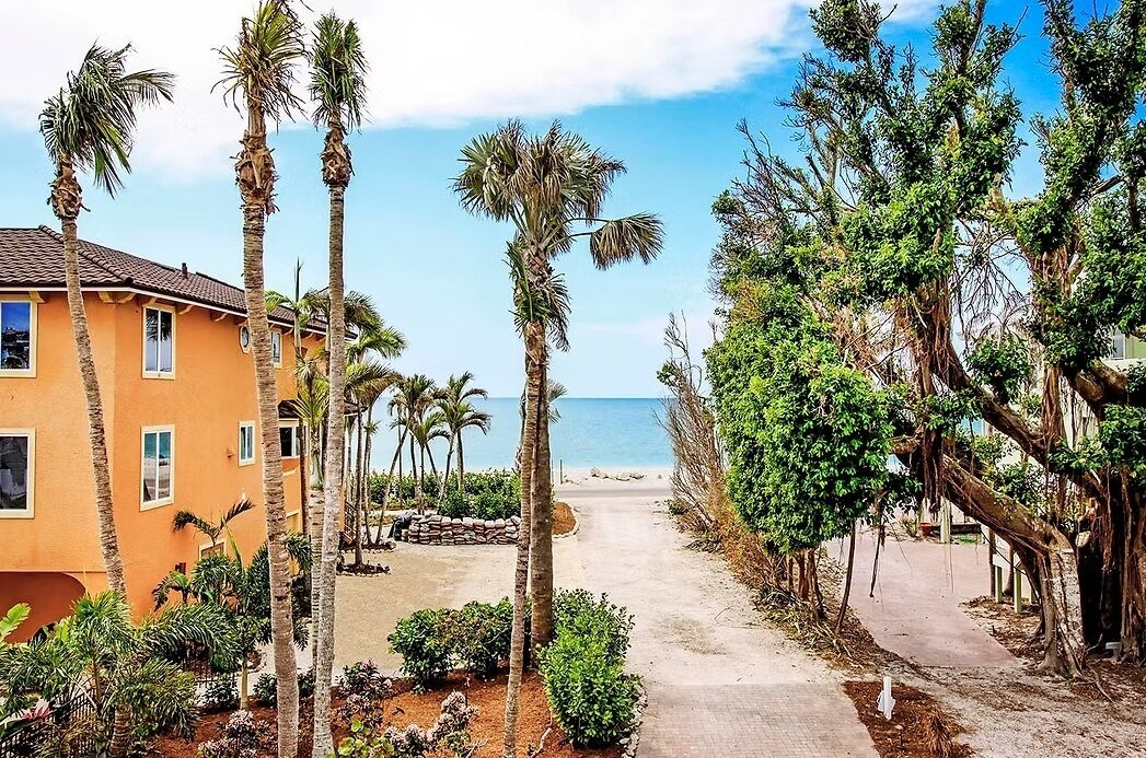 A pathway leading to a beach with palm trees and a building with a tiled roof.