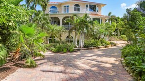 A two-story building with a red roof, surrounded by lush greenery and a paved pathway. - Luxury 5BR Gulf-View Home with Private Pool, Spa & High-Tech Entertainment (Captiva)