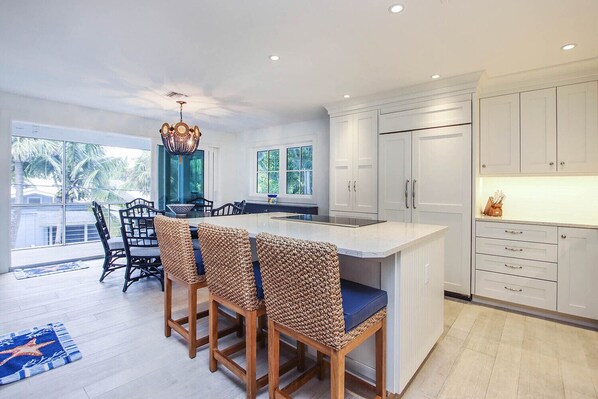 A modern kitchen with white cabinets, a central island with bar stools, and a large window overlooking a balcony.