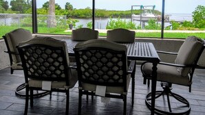 A patio with a table and chairs, overlooking a body of water and a dock. - Modern Waterfront Home with Hot Tub, Dock, Kayaks (New Port Richey)