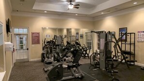 A gym with various exercise machines, a blue exercise ball, and a ceiling fan.