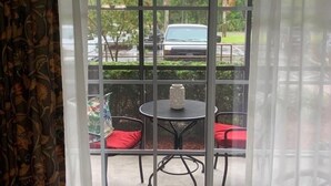 A view through a window with a patterned curtain, a patio with a table and chairs, and a car parked outside.