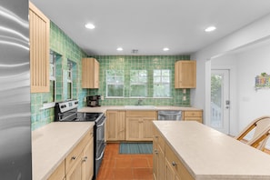 Una cocina con salpicadero de azulejos verdes, armarios de madera, una estufa y un lavavajillas.