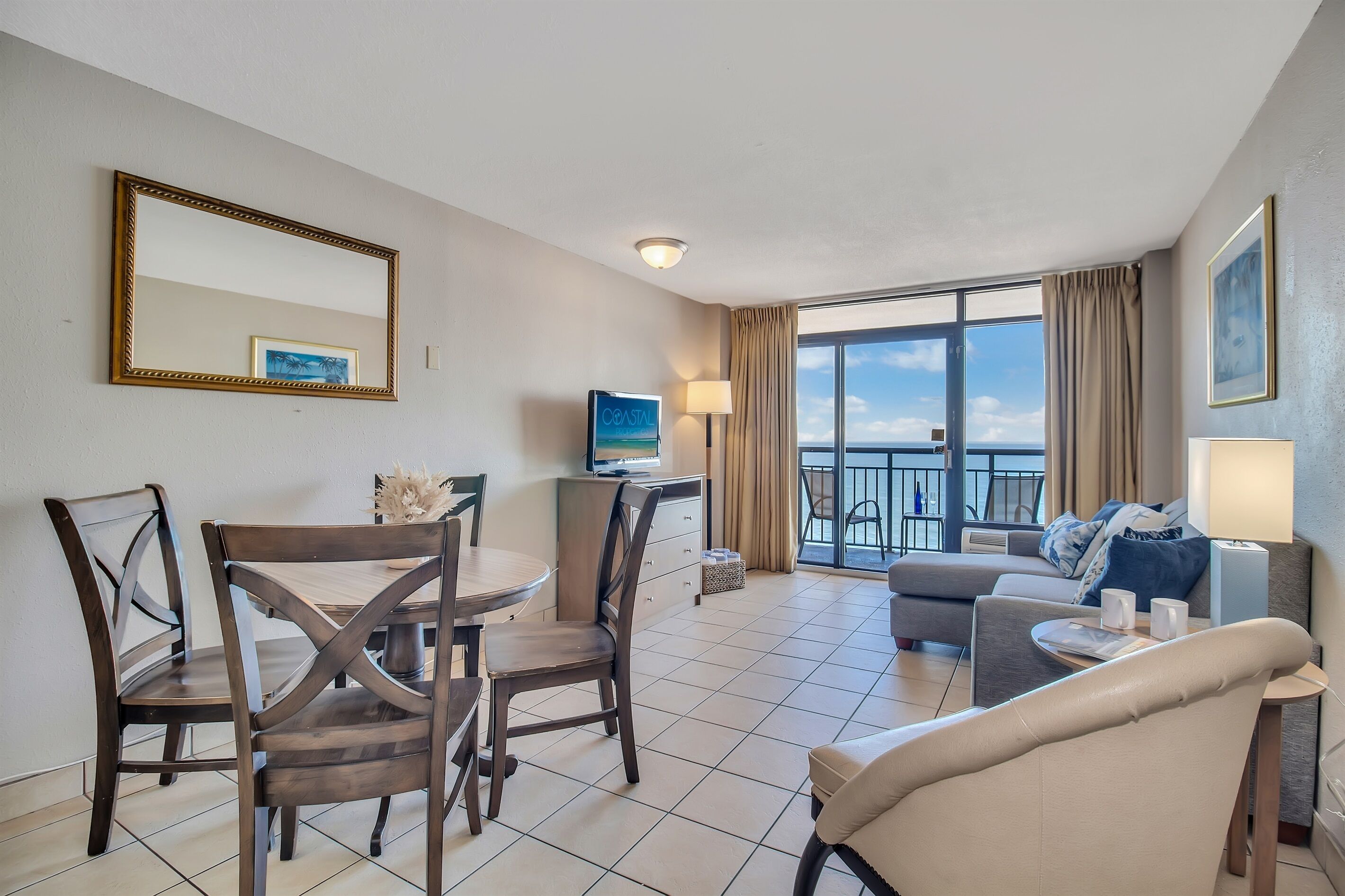 Habitación de hotel con comedor, sofá, televisión y balcón con vistas.