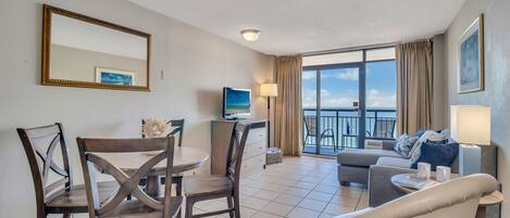 Habitación de hotel con comedor, sofá, televisión y balcón con vistas.