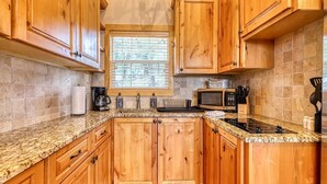 A kitchen with wooden cabinets, granite countertops, a window, and a microwave. - Lake Travis Waterfront with Resort Style Pool and Million Dollar Views. (Marble Falls)