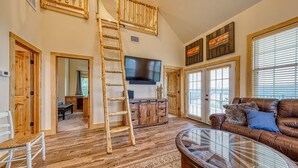A spacious living room with a wooden floor, a glass coffee table, a leather sofa, and a TV mounted on the wall. - Lake Travis Waterfront with Resort Style Pool and Million Dollar Views. (Marble Falls)