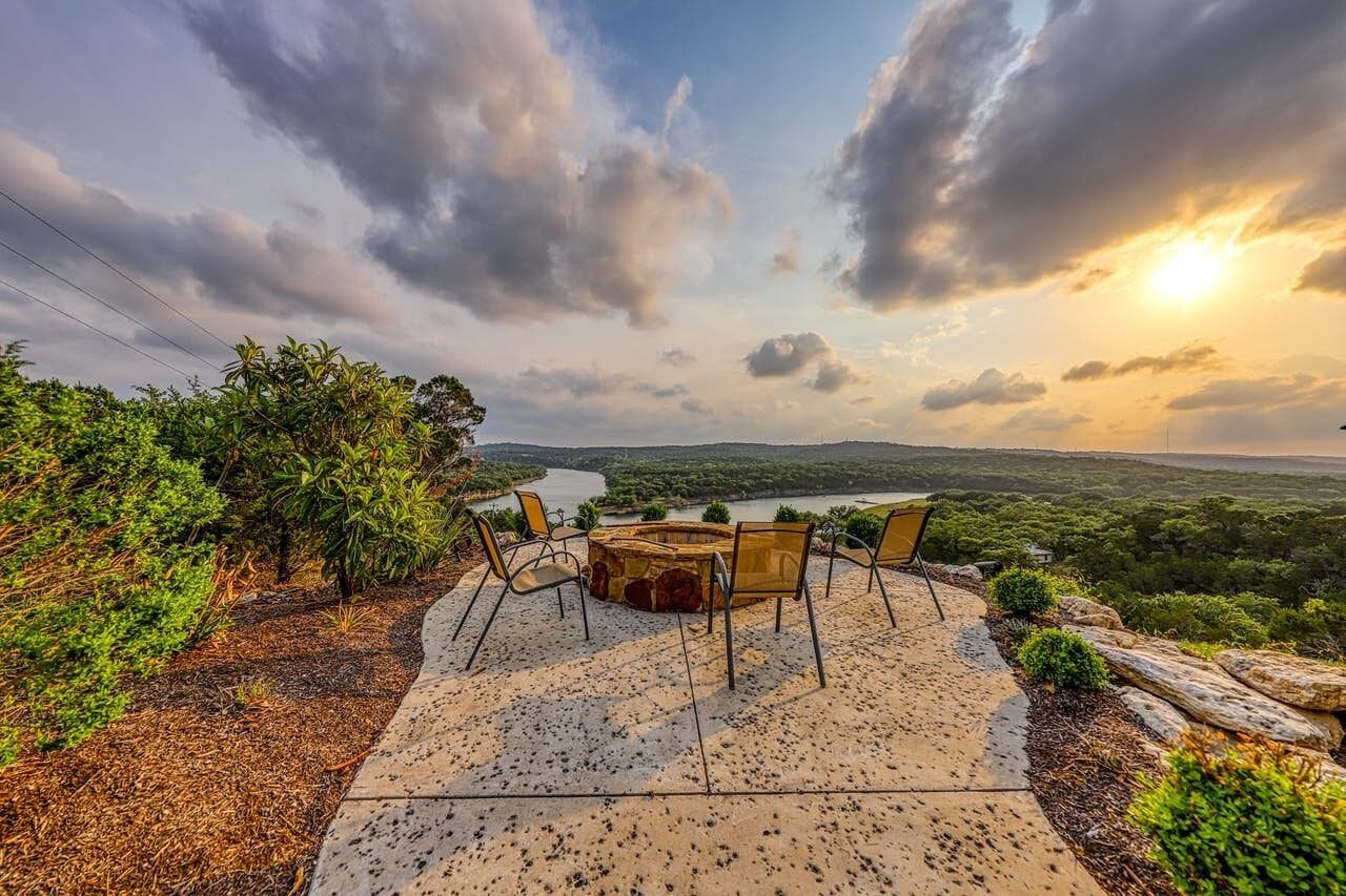 Un espace extérieur aménagé avec une table ronde et des chaises, offrant une vue sur une rivière et un paysage vallonné.