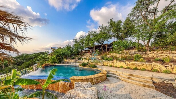 A pool surrounded by stone steps and greenery, with a clear sky above. - Lake Travis Waterfront with Resort Style Pool and Million Dollar Views. (Marble Falls)