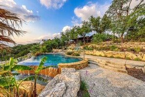 Una piscina rodeada de escalones de piedra y follaje, bajo un cielo despejado.
