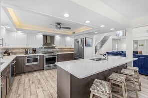 Una cocina moderna con una isla central, electrodomésticos de acero inoxidable y una escalera que lleva a un nivel superior.