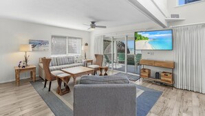 A spacious living room with a large TV, comfortable seating, and a balcony with a view of the ocean. - Renovated 6-Bedroom Beachfront Home with Ramp Access & Gulf Views (Captiva)
