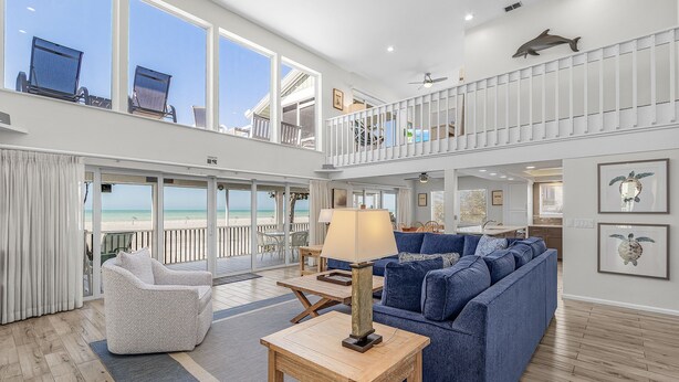 A spacious living area with a blue sofa, a patterned armchair, and a wooden coffee table. Large windows offer a view of the ocean. - Renovated 6-Bedroom Beachfront Home with Ramp Access & Gulf Views (Captiva)