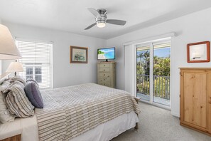 Un dormitorio con cama, televisor, ventilador de techo, ventana y balcón.