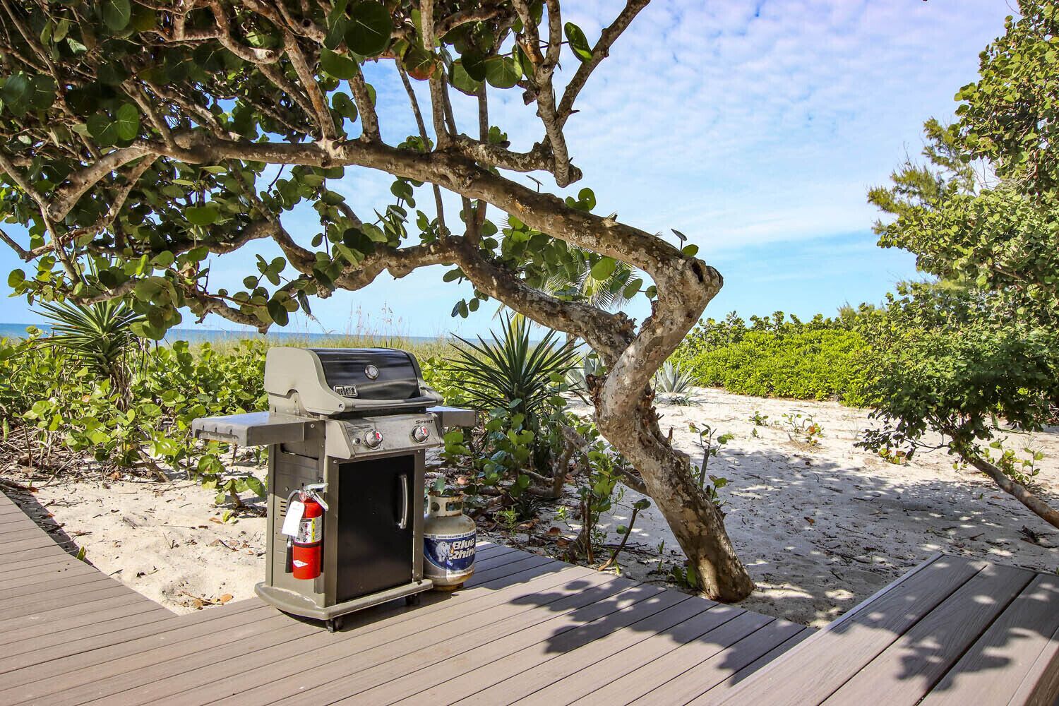 A barbecue grill on a wooden deck with a view of the beach and ocean.