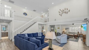 A spacious living area with a blue sofa, a wooden coffee table, and a staircase leading to an upper level. - Renovated 6-Bedroom Beachfront Home with Ramp Access & Gulf Views (Captiva)