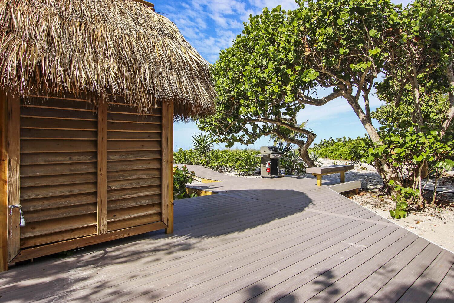 Una estructura de madera con techo de paja, una terraza de madera y vista a una playa y árboles.