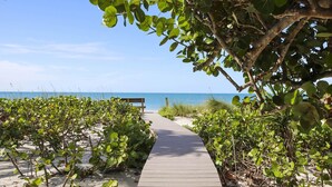 A wooden boardwalk leading to a beach with dense vegetation on either side. - Renovated 6-Bedroom Beachfront Home with Ramp Access & Gulf Views (Captiva)