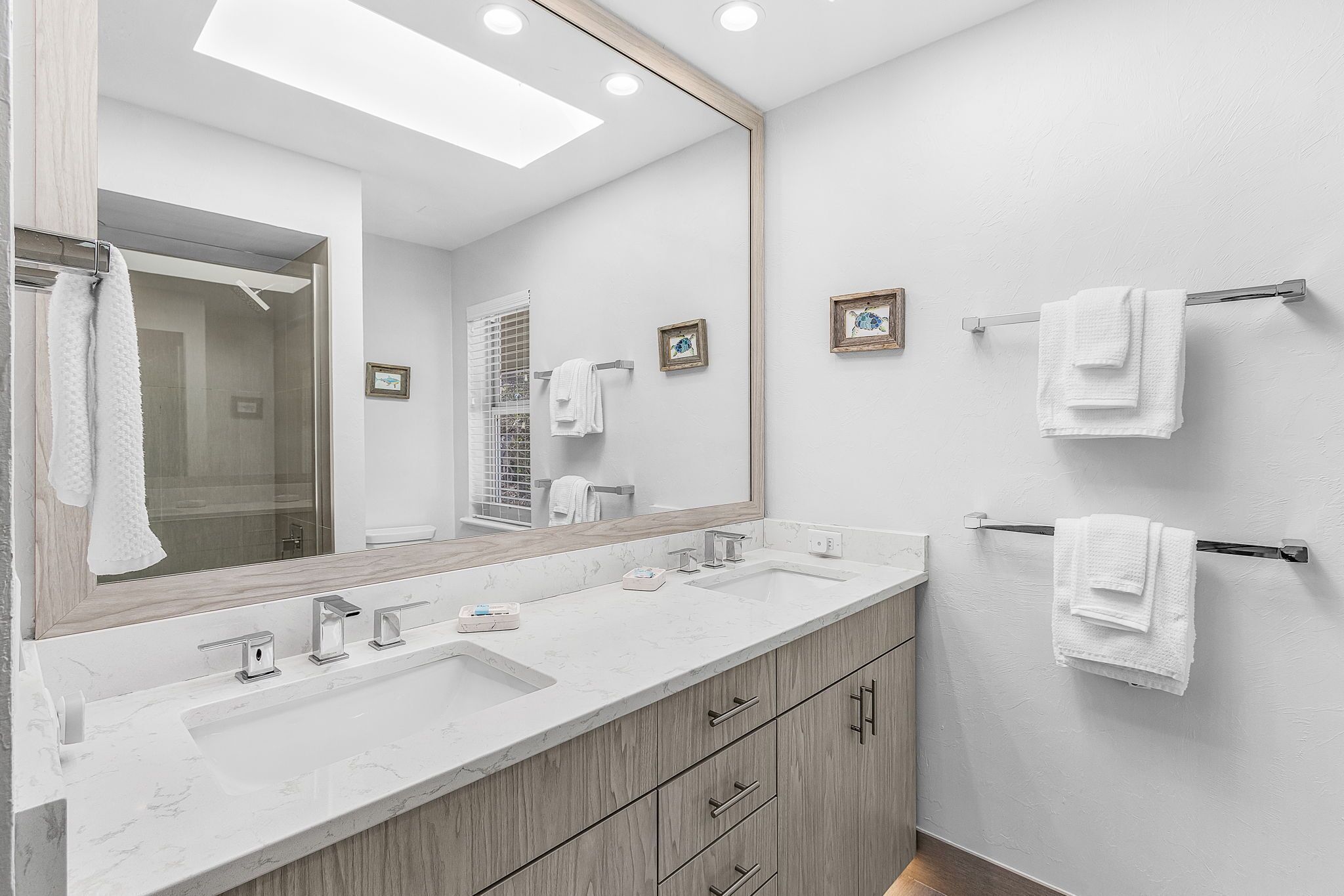 Un baño moderno con un espejo grande, dos lavamanos, armarios de madera y toallas blancas.