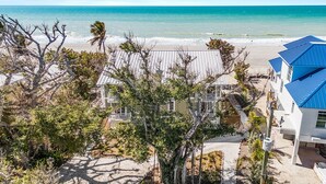 A beachfront property with a white building and a blue-roofed structure, surrounded by trees and a sandy beach. - Renovated 6-Bedroom Beachfront Home with Ramp Access & Gulf Views (Captiva)
