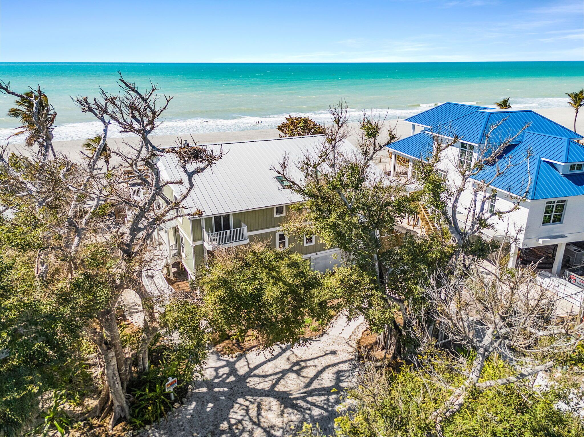 Une propriété située en bord de mer, avec un bâtiment au toit bleu, un bâtiment blanc et une plage de sable.