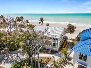 Una propiedad frente a la playa con una casa grande, un edificio más pequeño y una estructura de techo azul.
