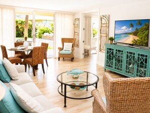 A living room with wicker furniture, a glass coffee table, and a television displaying a beach scene.