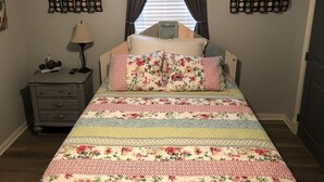 Un dormitorio con cama, mesita de noche, lámpara y dos adornos en la pared.