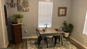 Un comedor con mesa, sillas, candelabro y plantas en macetas.