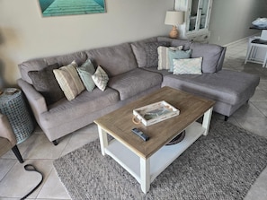 Un salon avec un canapé d’angle gris, une table basse en bois et un tapis gris.