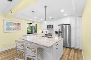 Una cocina con una isla grande, muebles blancos, electrodomésticos de acero inoxidable y un cuadro en la pared.