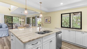 Una cocina amplia con una isla grande, muebles blancos y un comedor con sofá azul.