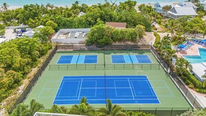 Una cancha de tenis con piscina y vista al mar.
