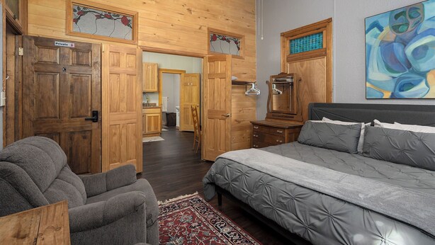 Une chambre à coucher avec un lit, une chaise, des portes en bois et un couloir menant à une salle de bain.