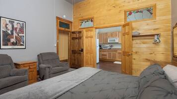 Een kamer met een bed, twee fauteuils, een houten wand, een keukenhoek en een lijst met een foto.