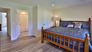 A bedroom with a wooden bed, a nightstand, and a lamp. There are two doors and a hallway leading to another room.