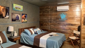 A hotel room with two beds, wooden walls, a mounted air conditioner, and a buffalo logo on the wall. - 5 Cabins at The Lazy Buffalo, Wichita Mountains Cache Lawton Fort Sill sleeps 16 (Cache)