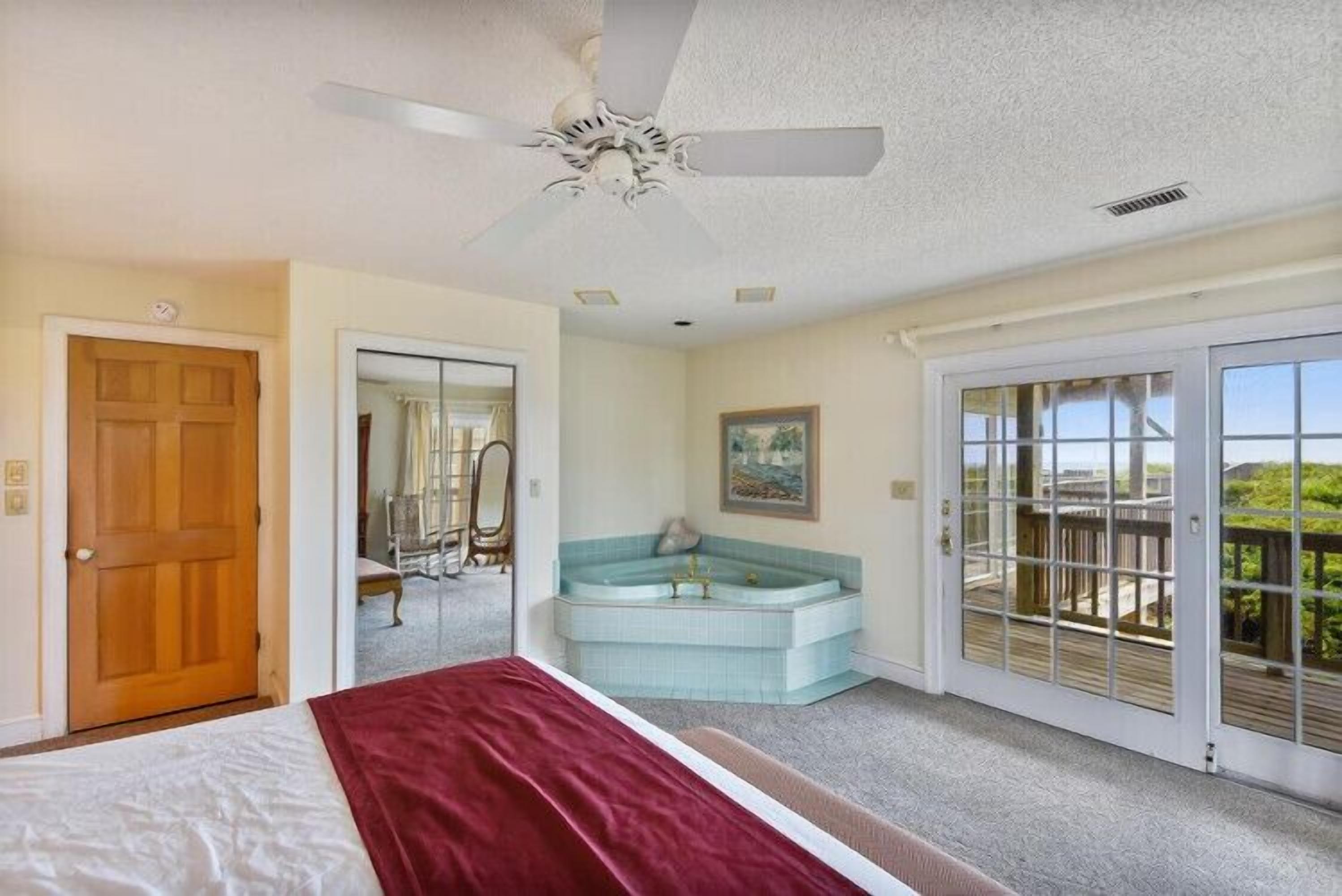 Une chambre à coucher comprenant un lit, un ventilateur de plafond, une porte-fenêtre coulissante donnant sur un balcon et un jacuzzi.