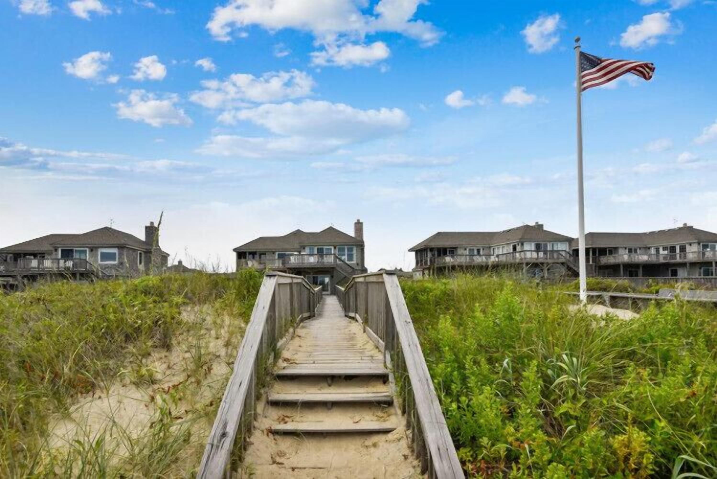 A wooden boardwalk leading to beach houses with a flagpole.