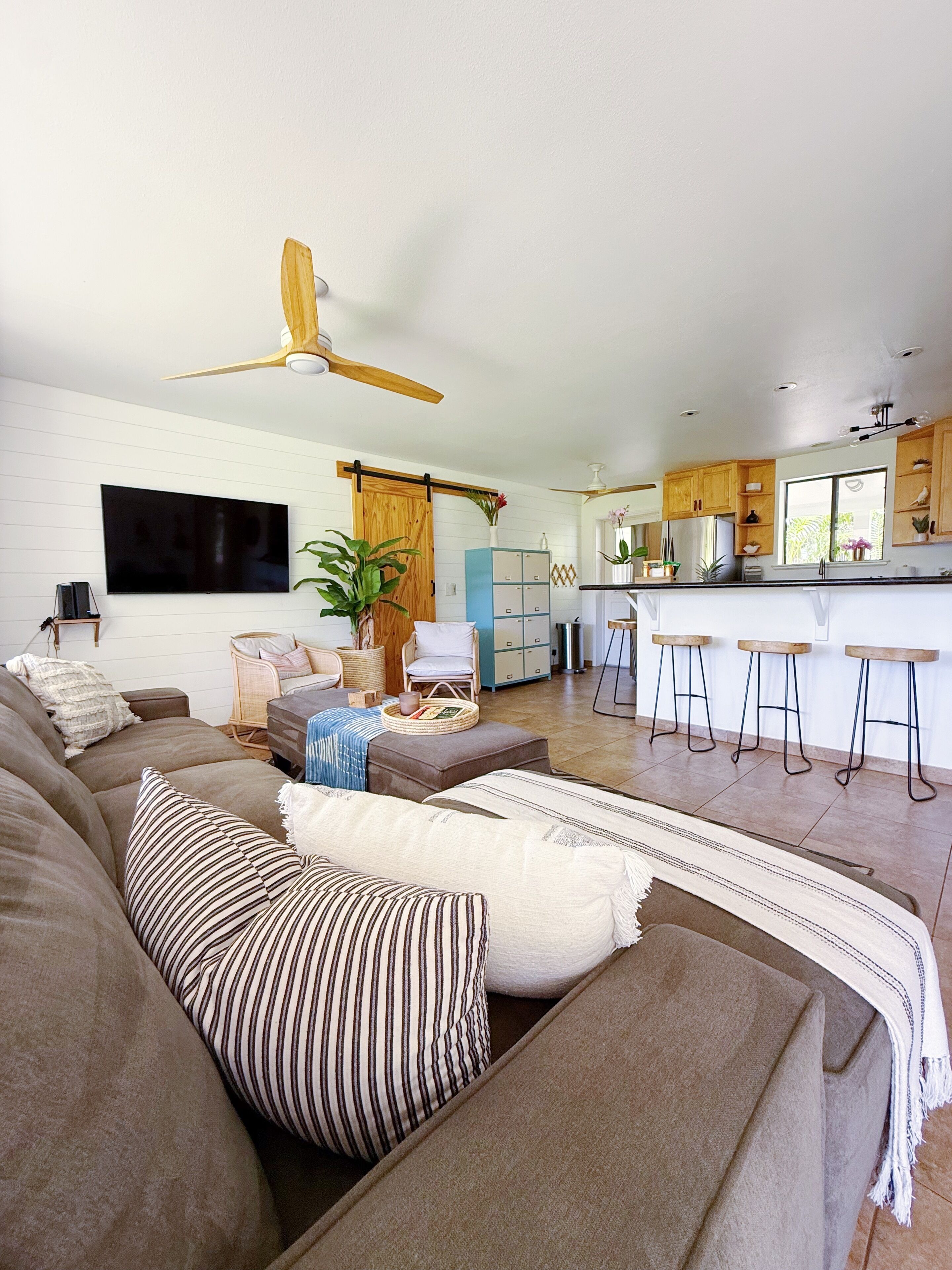 Una sala de estar moderna con un sofá grande, una mesa de centro y un televisor. Hay una zona de cocina con una barra y taburetes.