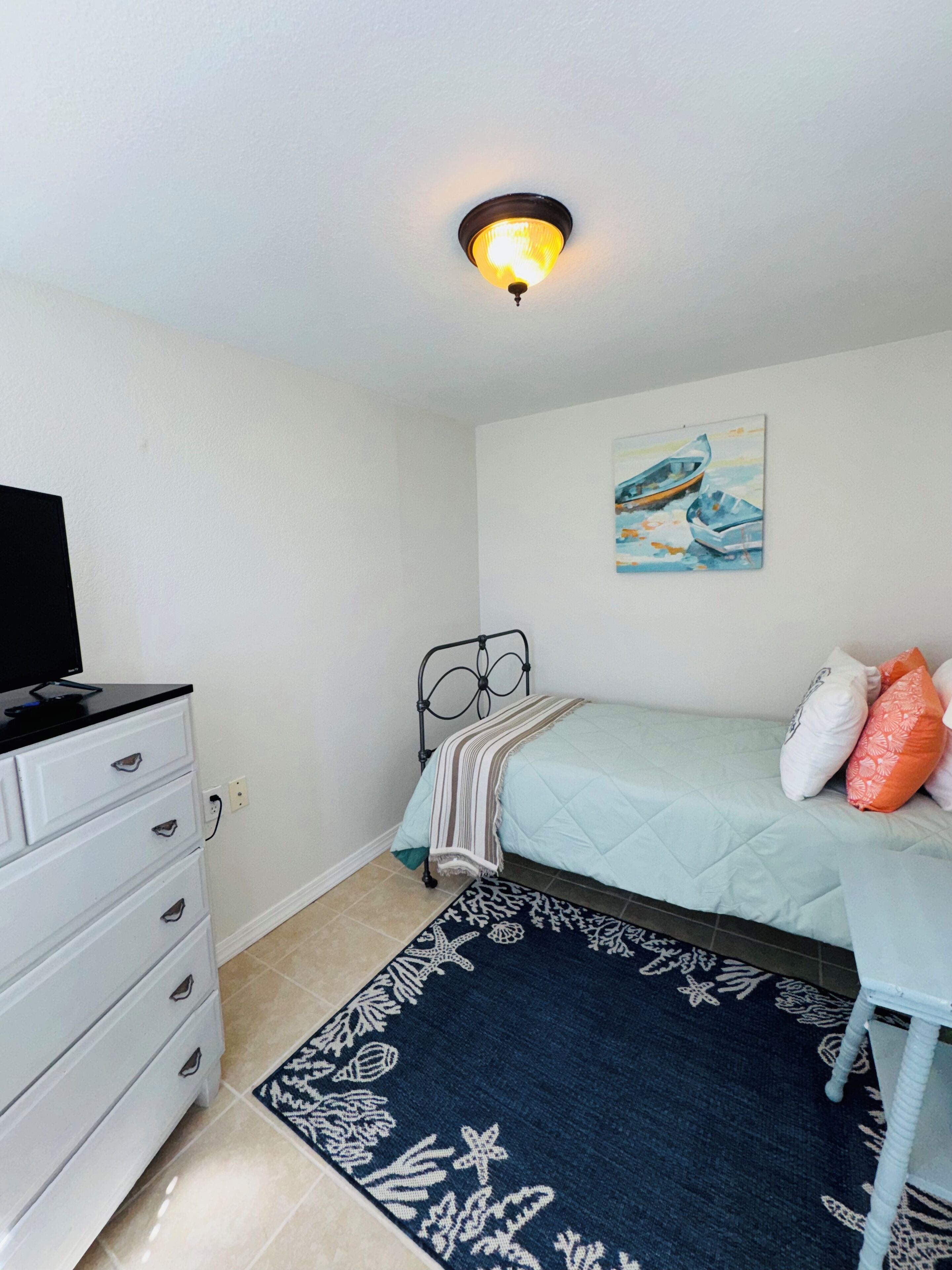 Une chambre à coucher avec un lit, une commode, un tableau et un luminaire au plafond.