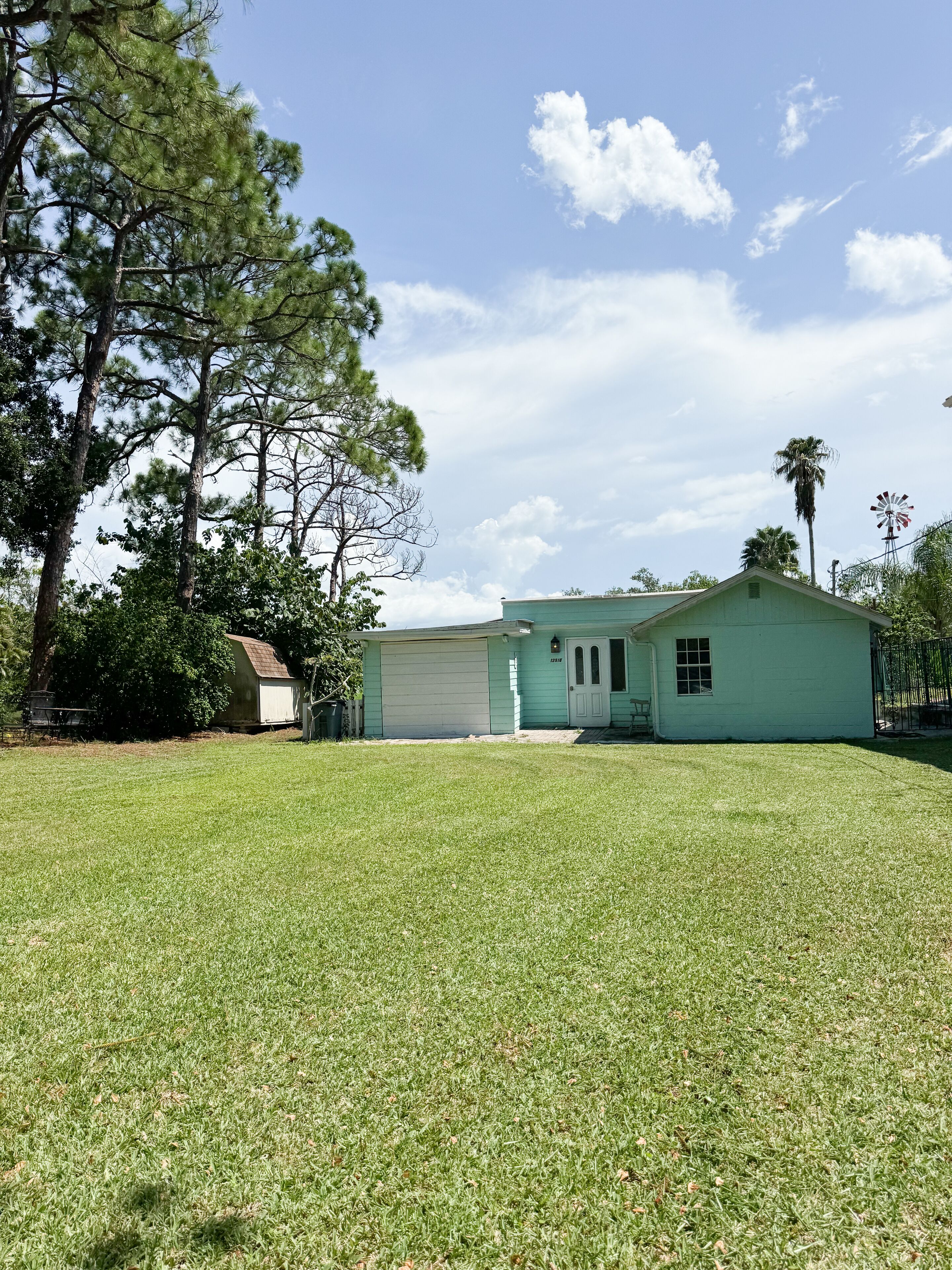 A single-story house with a garage, surrounded by a well-maintained lawn and tall trees.