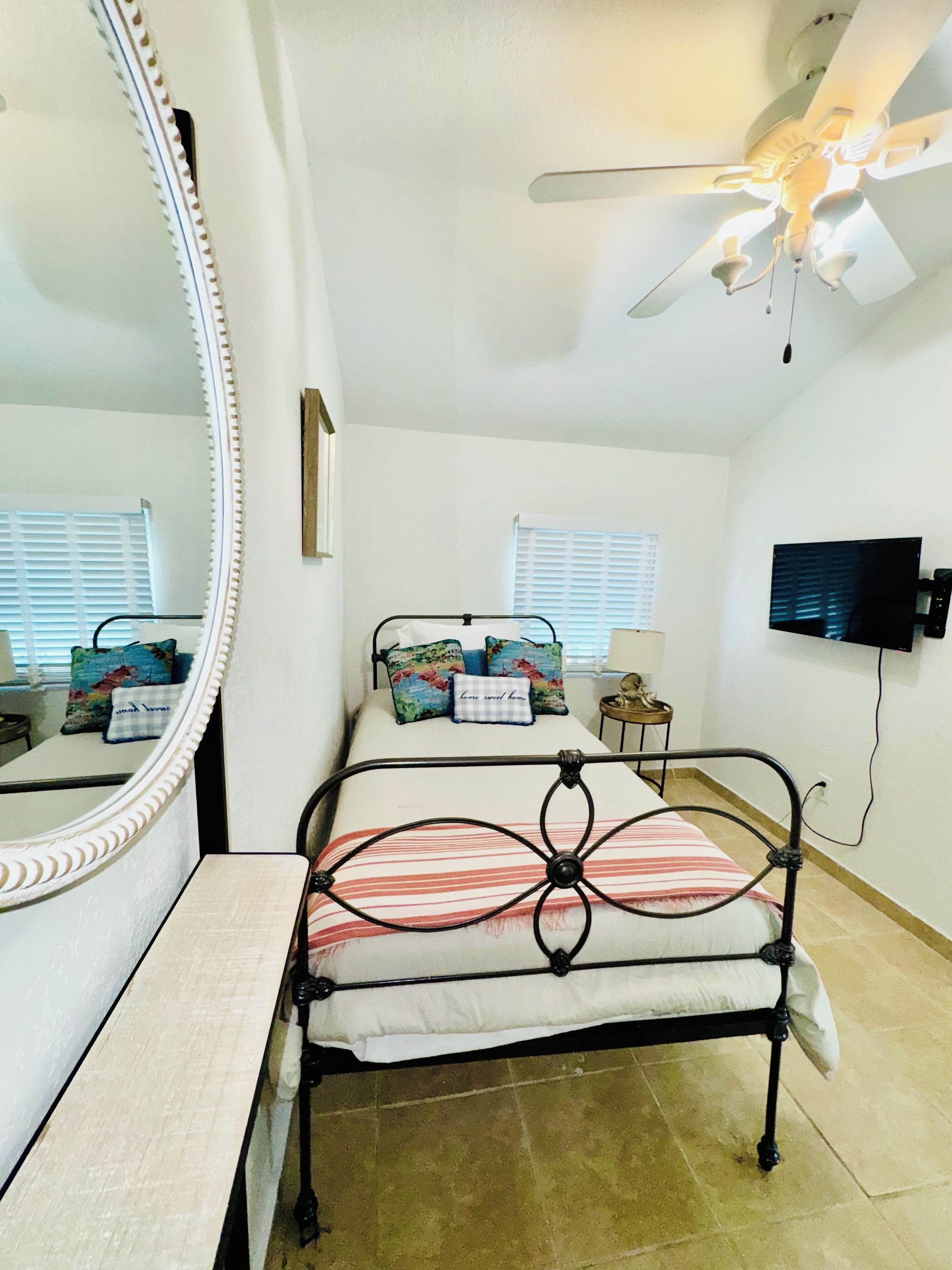 A bedroom with a bed, a ceiling fan, a TV, and a large mirror.