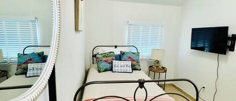 A bedroom with a bed, a ceiling fan, a TV, and a large mirror.