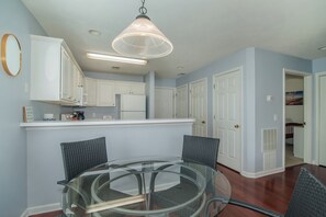 A dining area with a glass table and chairs, a hanging light fixture, white cabinets, and a door leading to another room.