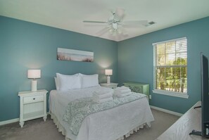 A bedroom with a bed, nightstands, a ceiling fan, a window with blinds, and a painting on the wall.