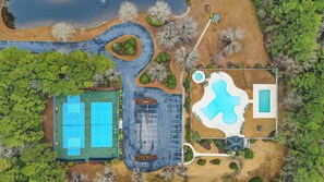 An aerial view of a property with a tennis court, a swimming pool, and surrounding landscaping.